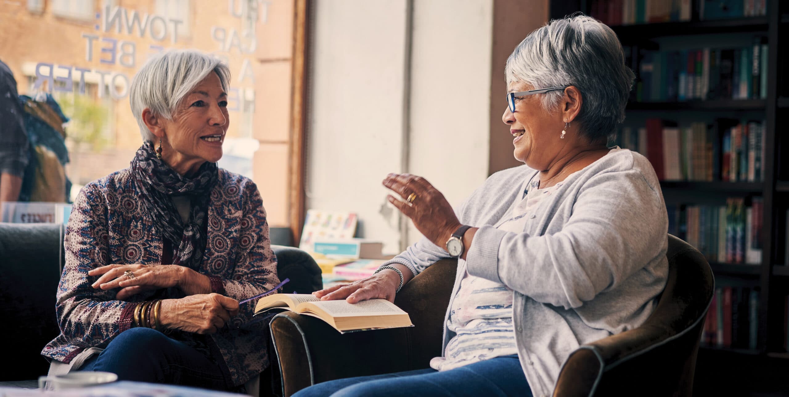Two older women engage in intellectual discussion in a library.
